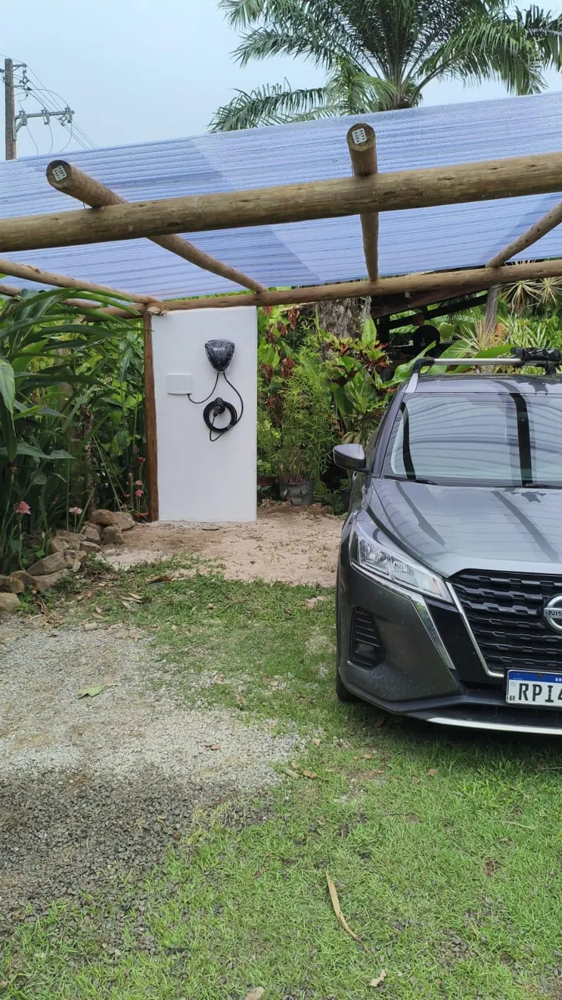 Veículo elétrico em recarga em carregador de parede sob pergolado de residência